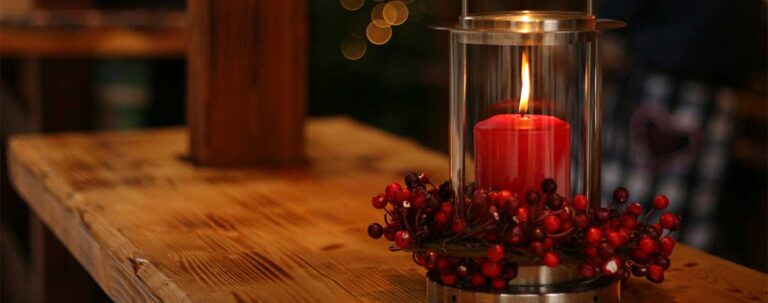 Rote Kerze in Lampe mit roten Früchtedeko