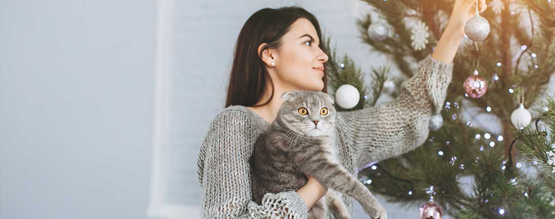 Frau mit Katze im Arm vor Weihnachtsbaum