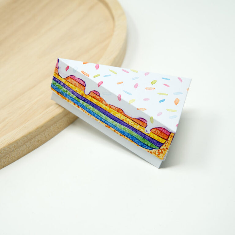 Papier Tortenstück mit Regenbogen Schichte steht schräg auf Holzplatte