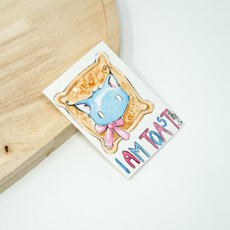 Handgezeichnete ACEO Karte mit blauem Kater Pumpkin, dessen Kopf durch einen Toast gesteckt ist, mit rosa Schleife und buntem Schriftzug I am Toast in Aquarell.