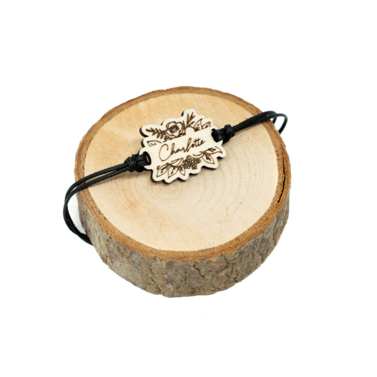 Verstellbares schwarzes Kordel-Armband mit lasergeschnittenem Holzanhänger in Blumenform mit graviertem Wunschnamen Charlotte auf hellem Holzhintergrund.