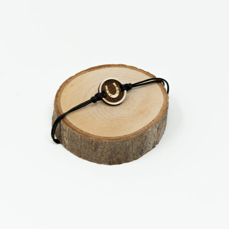 Verstellbares schwarzes Kordel-Armband mit rundem Holzanhänger und graviertem Hufeisen-Motiv auf hellem naturbelassenem Holzhintergrund.