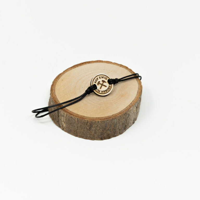 Verstellbares schwarzes Kordel-Armband mit rundem Holzanhänger und graviertem Hacke-Schlegel-Symbol mit Schriftzug Auf ewig im Herzen auf hellem naturbelassenem Holzhintergrund.